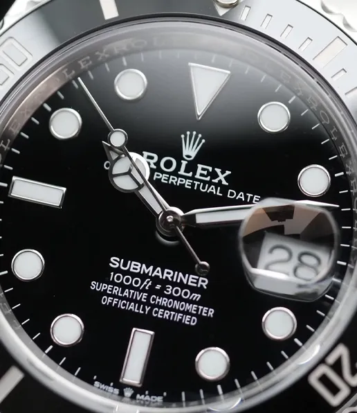 Close-up of a Rolex Submariner watch face showing the date as 28, with white hour markers, silver hands, and the Oyster Perpetual Date and Superlative Chronometer labels clearly visible.