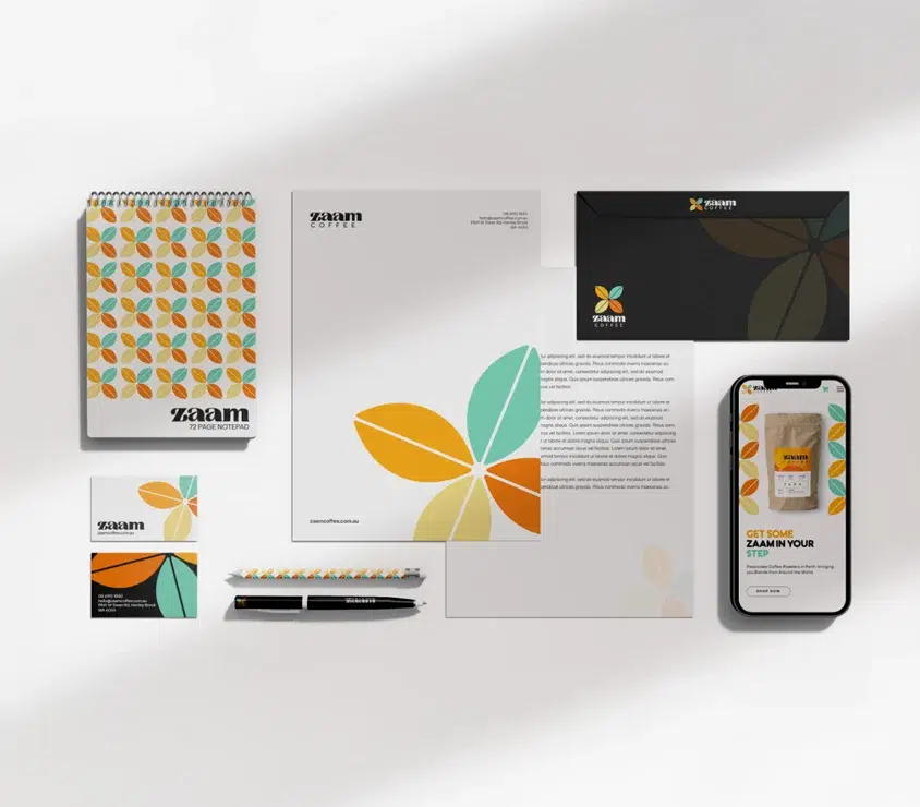 A stationery set with colourful leaf patterns, including a notebook, notepad, pens, pencil, business card, letterhead, envelope, and a smartphone displaying a matching design. The branding reads ZAAM.
