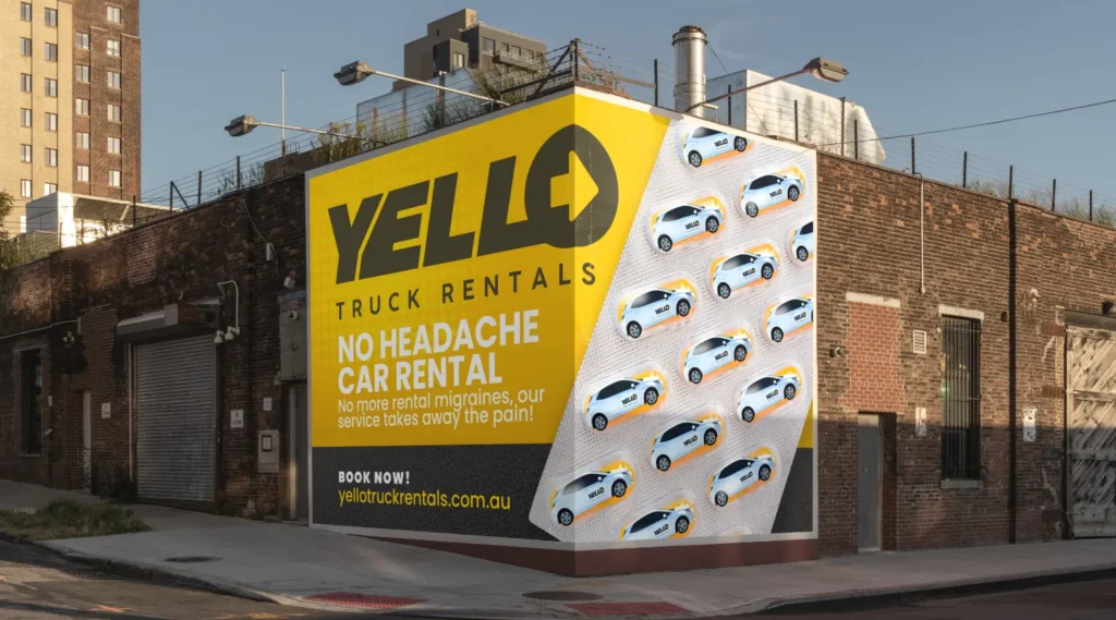 A large yellow and white billboard for Yello Truck Hire is mounted on a brick building. The advert features the slogan No Headache Car Hire and images of multiple small cars.