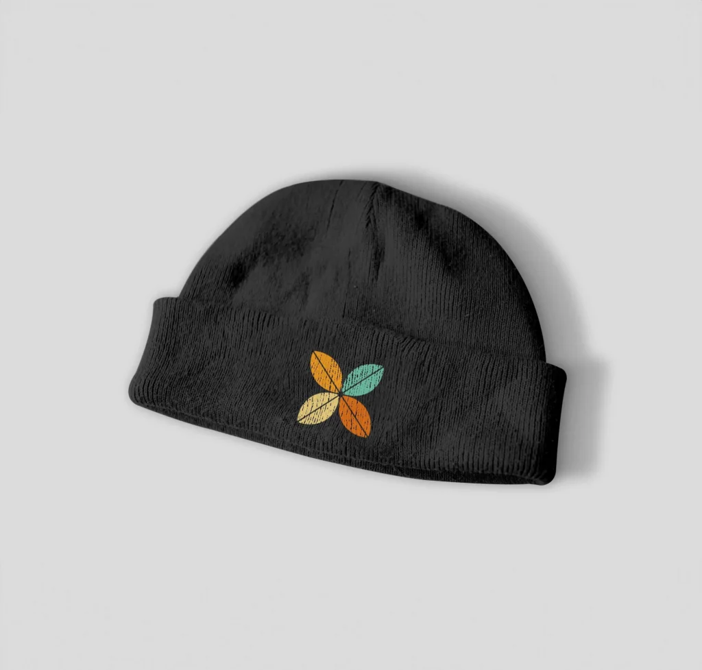 A black beanie hat with a colourful four-leaf design embroidered on the front, featuring yellow, green, and orange leaves—perfect for coffee lovers and Zaam Coffee fans—displayed on a light grey background.