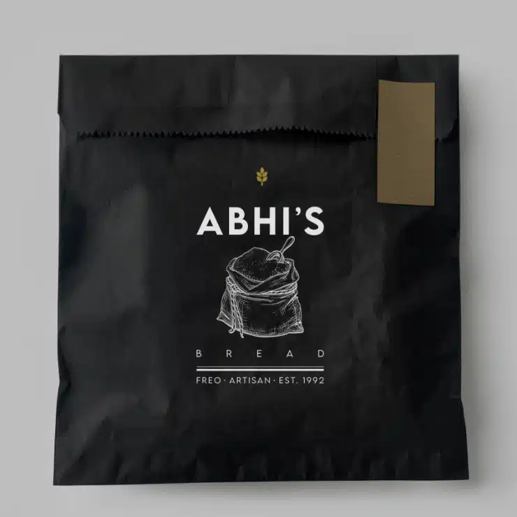A black paper bag from Abhi’s Bread bakery, printed in white with a sketch of a loaf of bread in a sack. Below it reads Freo . Artisan . Est. 1992. The bag is sealed with a gold sticker.