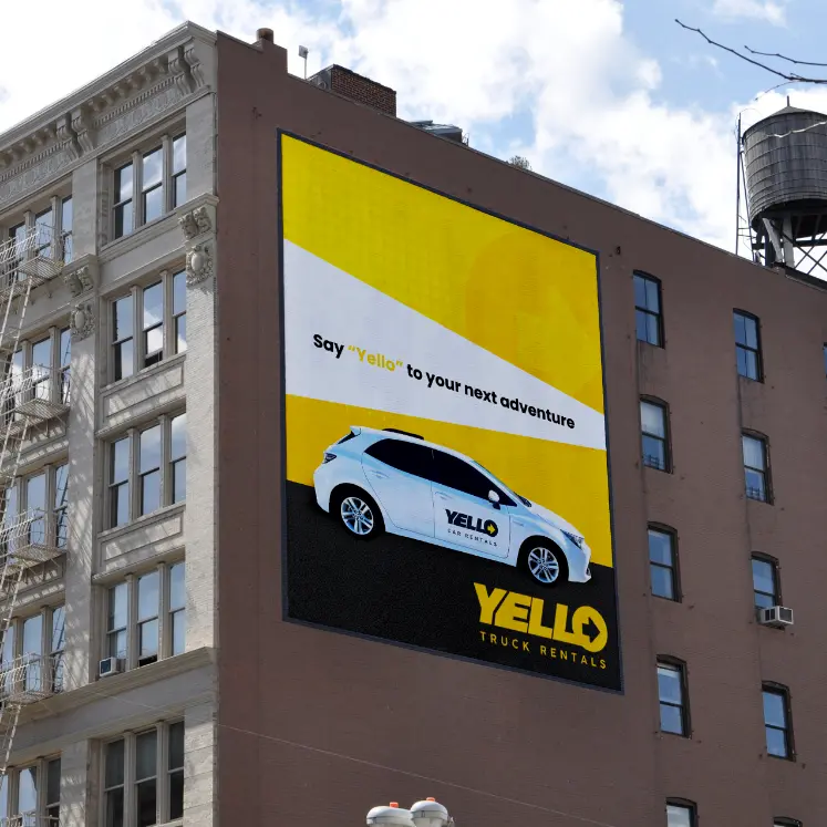 A large hoarding on a building displays a white car with YELLO branding and text saying, “Say ‘Yello’ to your next adventure.” At the bottom, the YELLO Truck Hire logo stands out against a bold yellow background.