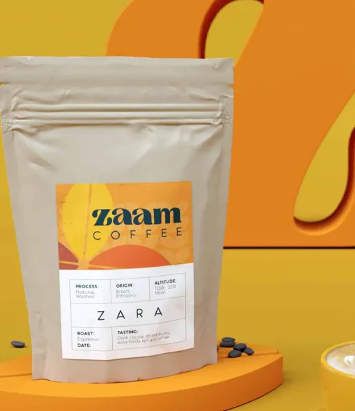 A beige bag of Zaam Coffee is displayed on a yellow surface with a yellow and orange abstract background. The label highlights details about the coffee’s origin, roast, and tasting notes, showcasing Zaam Coffee’s passion for expert coffee roasting. A cup sits in front.