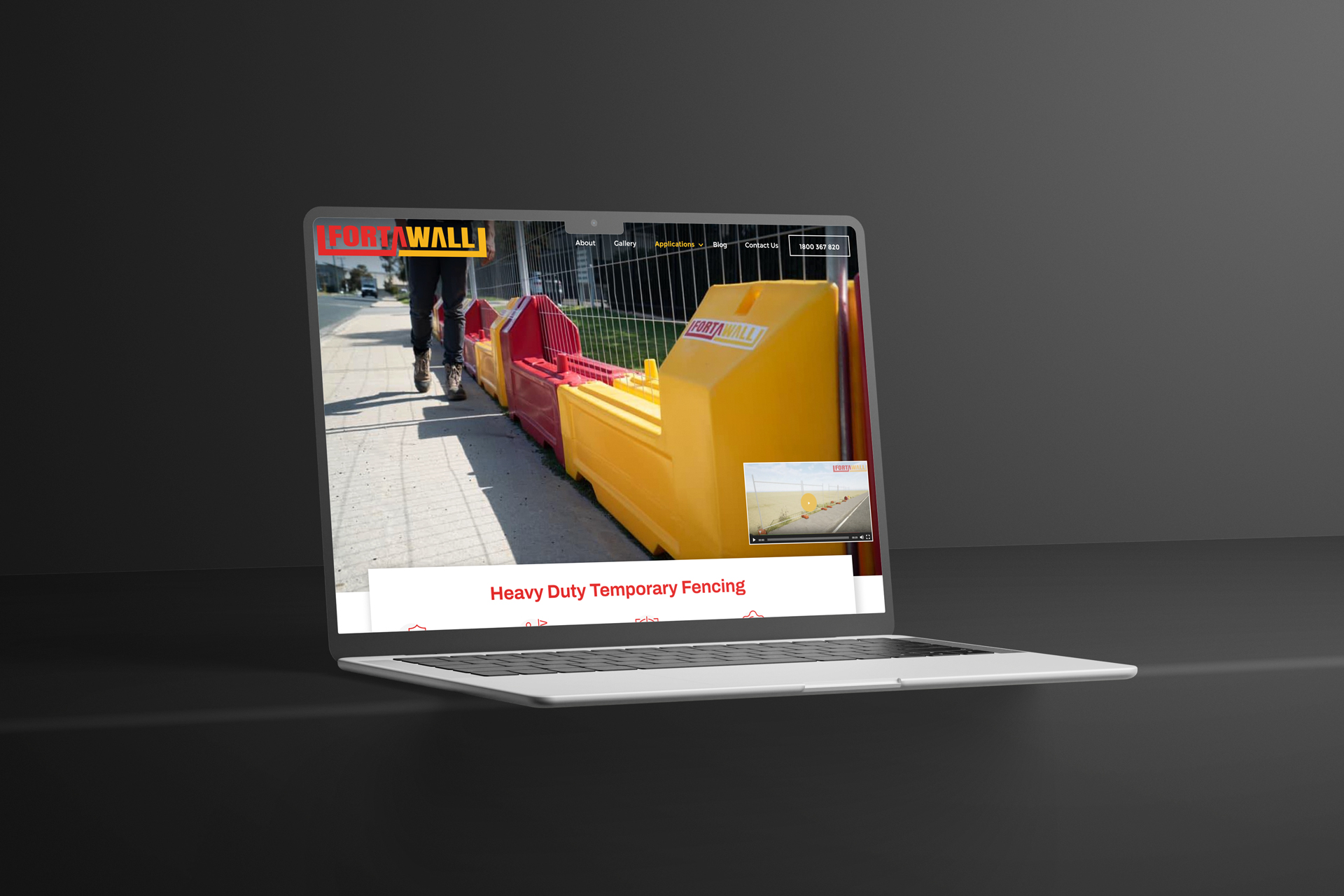 A laptop displays a website featuring heavy-duty temporary fencing with an image of yellow and red barriers along a pavement. The background is a plain, dark surface.
