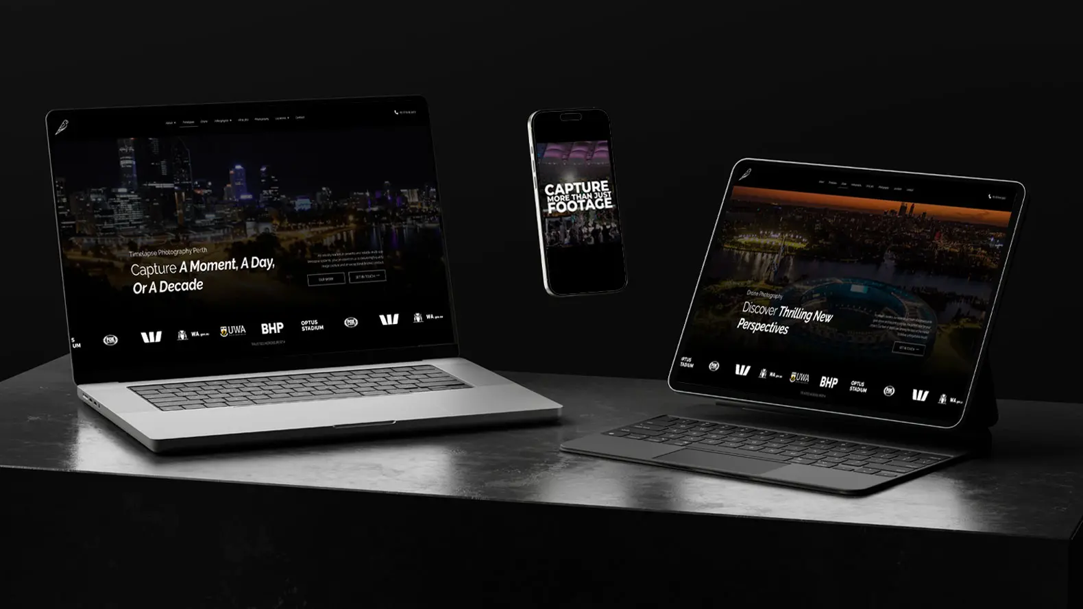 A laptop, tablet, and smartphone display similar dark-themed websites with cityscape images on a black surface and background, showcasing Birds Eye Media’s responsive web design across devices.