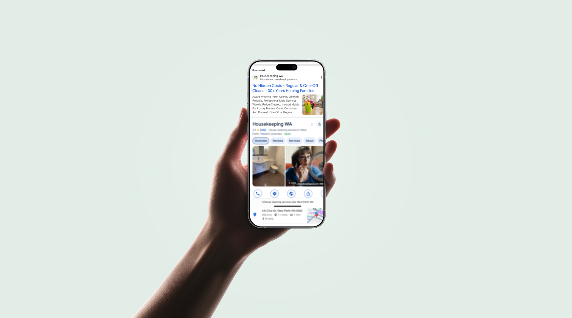 A hand holds a mobile displaying a search results page for Housekeeping WA, featuring links, photos of cleaning staff, and Cleaning Services options against a plain light background.