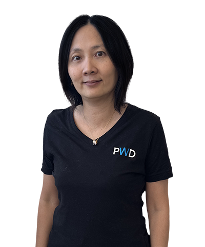 A woman with straight, shoulder-length black hair stands against a plain white background. She is wearing a black T-shirt with the letters PWD in blue and white on the left side of her chest.