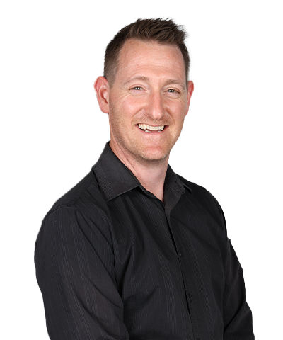 Chris Merton, a man with short light brown hair and fair skin, smiles whilst wearing a black button-up shirt. He is standing against a plain white background.