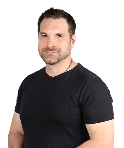 Chris Messina, a man with short dark hair and a beard, wearing a black T-shirt and a chain necklace, stands against a plain light background, smiling slightly at the camera.