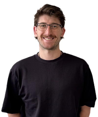 A smiling man with short brown hair, glasses, and a moustache is wearing a black T-shirt and standing against a plain white background.