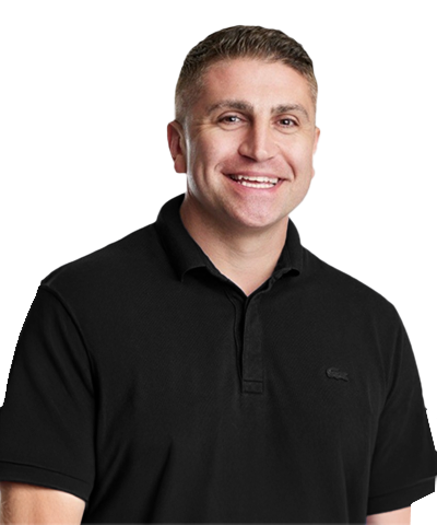 A man with short light brown hair, wearing a black collared shirt, is smiling and posing against a plain white background.