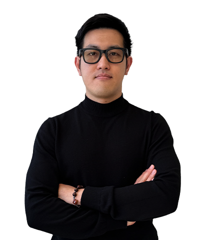 A person wearing black glasses and a black polo-neck jumper stands with arms crossed, looking confidently at the camera against a plain white background.