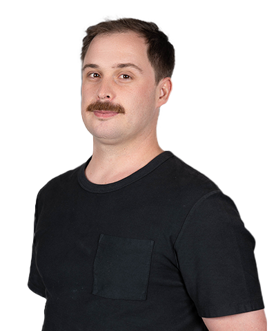 Warrun Lewis, a man with short brown hair and a moustache, is wearing a black T-shirt. He stands against a plain white background, looking slightly to the side with a neutral expression.