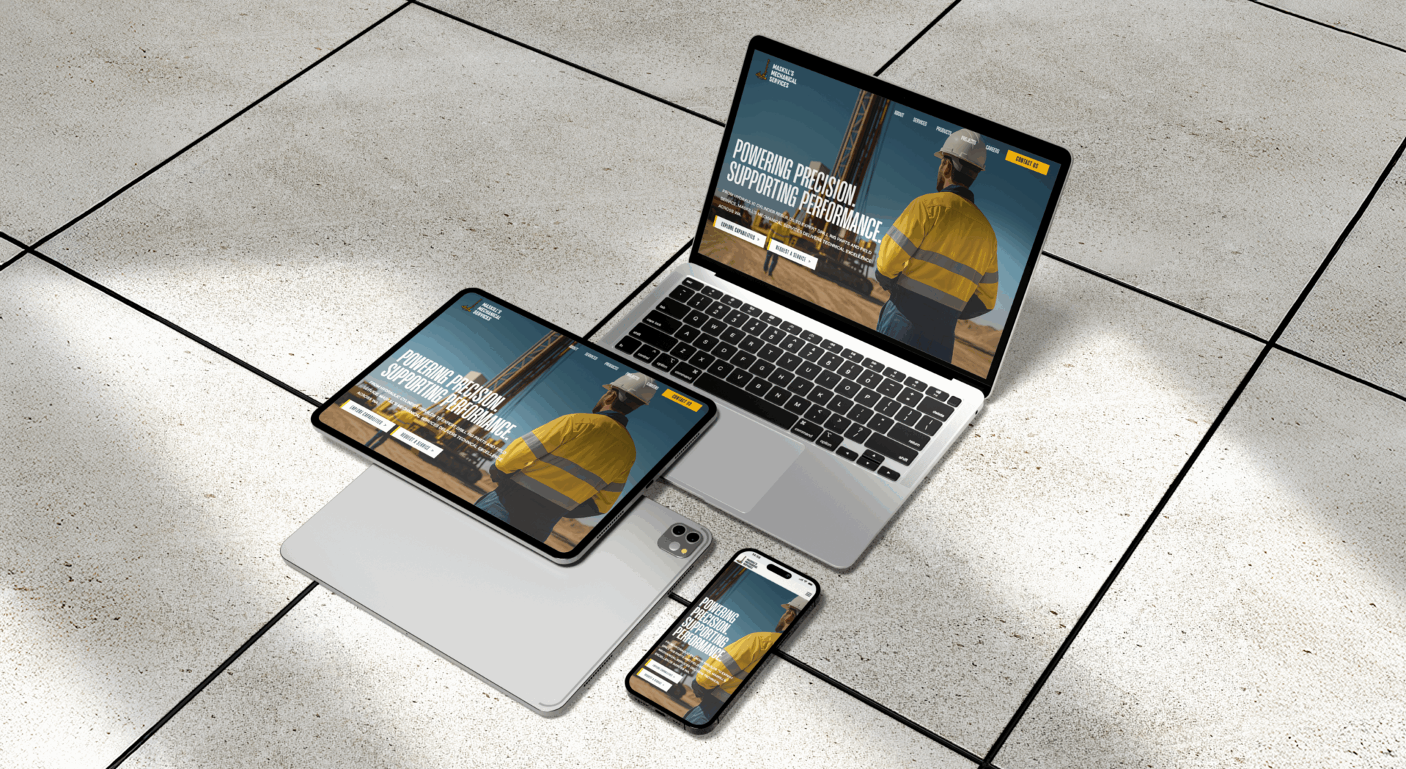 A laptop, tablet, and smartphone display the Maskills Mechanical Services website featuring a worker in a safety vest and helmet, all arranged on a tiled floor next to a closed laptop.