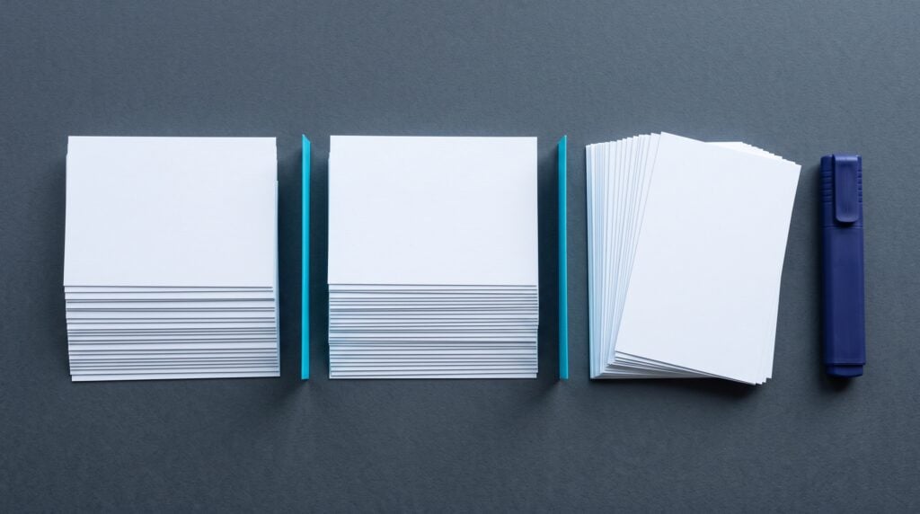 Blank white index cards sorted into three tidy stacks on a charcoal table with a cyan divider and an indigo highlighter