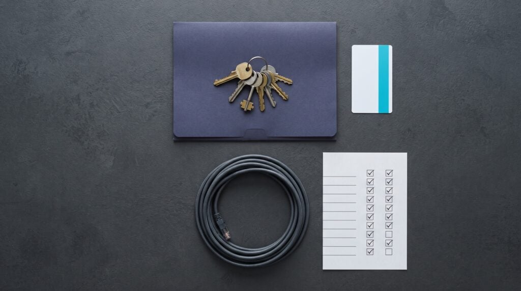 Set of keys, a notebook, a cable and a handover checklist laid out on a desk